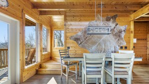 A wooden cabin interior with a dining area, large windows, and a hanging light fixture. - 20-Mile View, Hot Tub, Game Room, Waterfall (Sevierville)