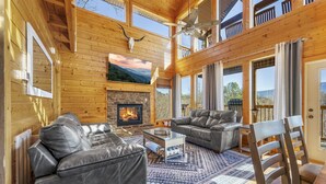 A cozy log cabin interior with a fireplace, leather sofas, and a large TV. - 20-Mile View, Hot Tub, Game Room, Waterfall (Sevierville)