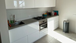 A modern kitchen with white cabinets, a gas stove, a sink, and a trash can.