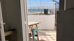 A room with a sliding glass door leading to a balcony with a view of the sea and a metal railing.
