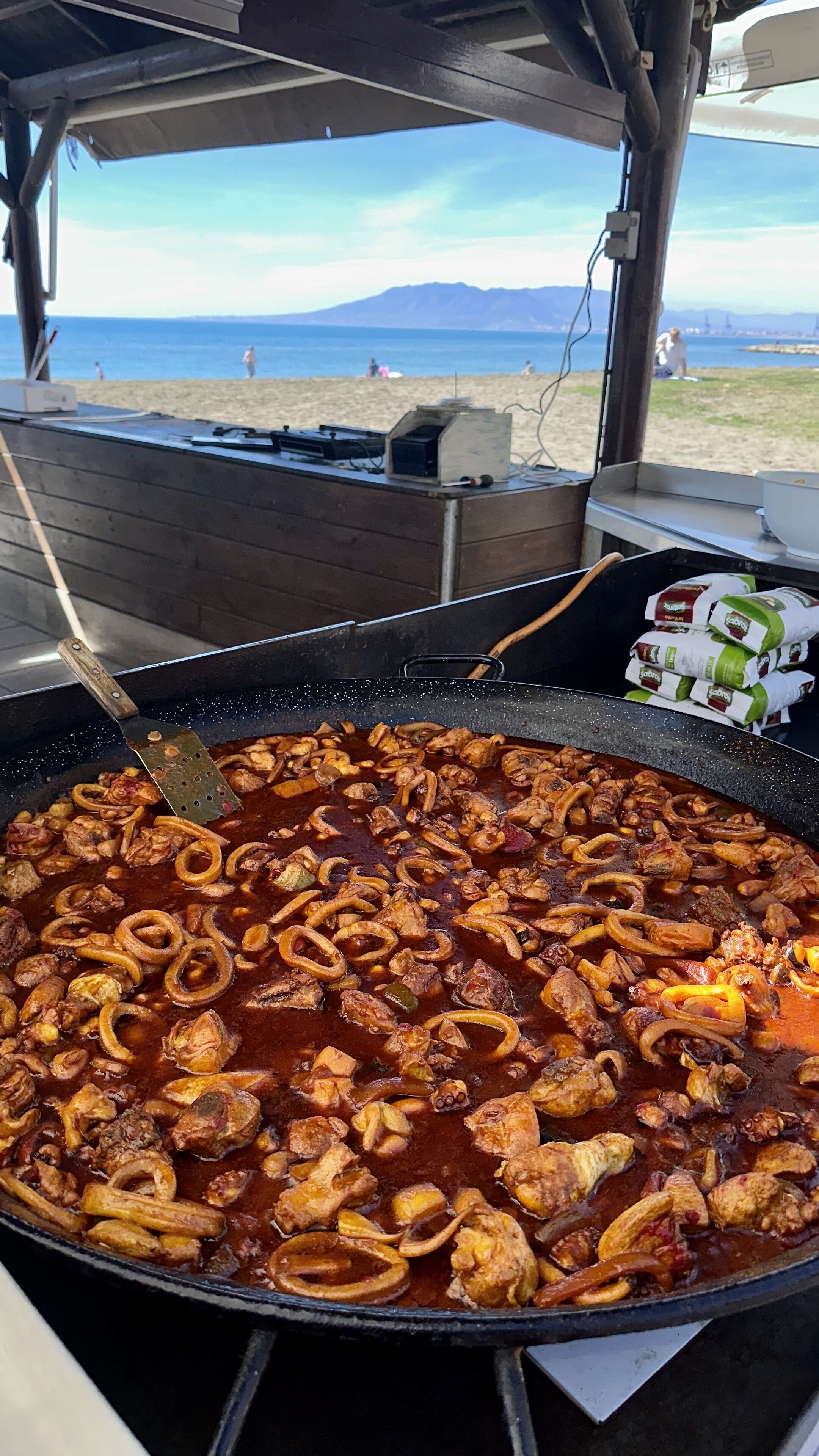 Ein großer Außenbereich zum Kochen mit Blick auf einen Strand und dahinter Berge.