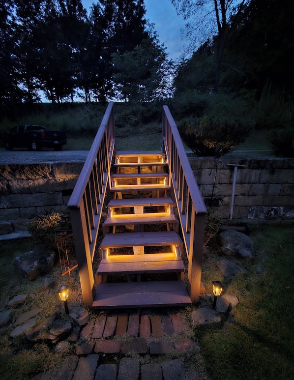 A wooden staircase with railings leading up to a higher level, surrounded by grass and rocks.