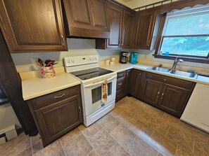 A kitchen with wooden cabinets, a white stove, a coffee maker, and a window with blinds.
