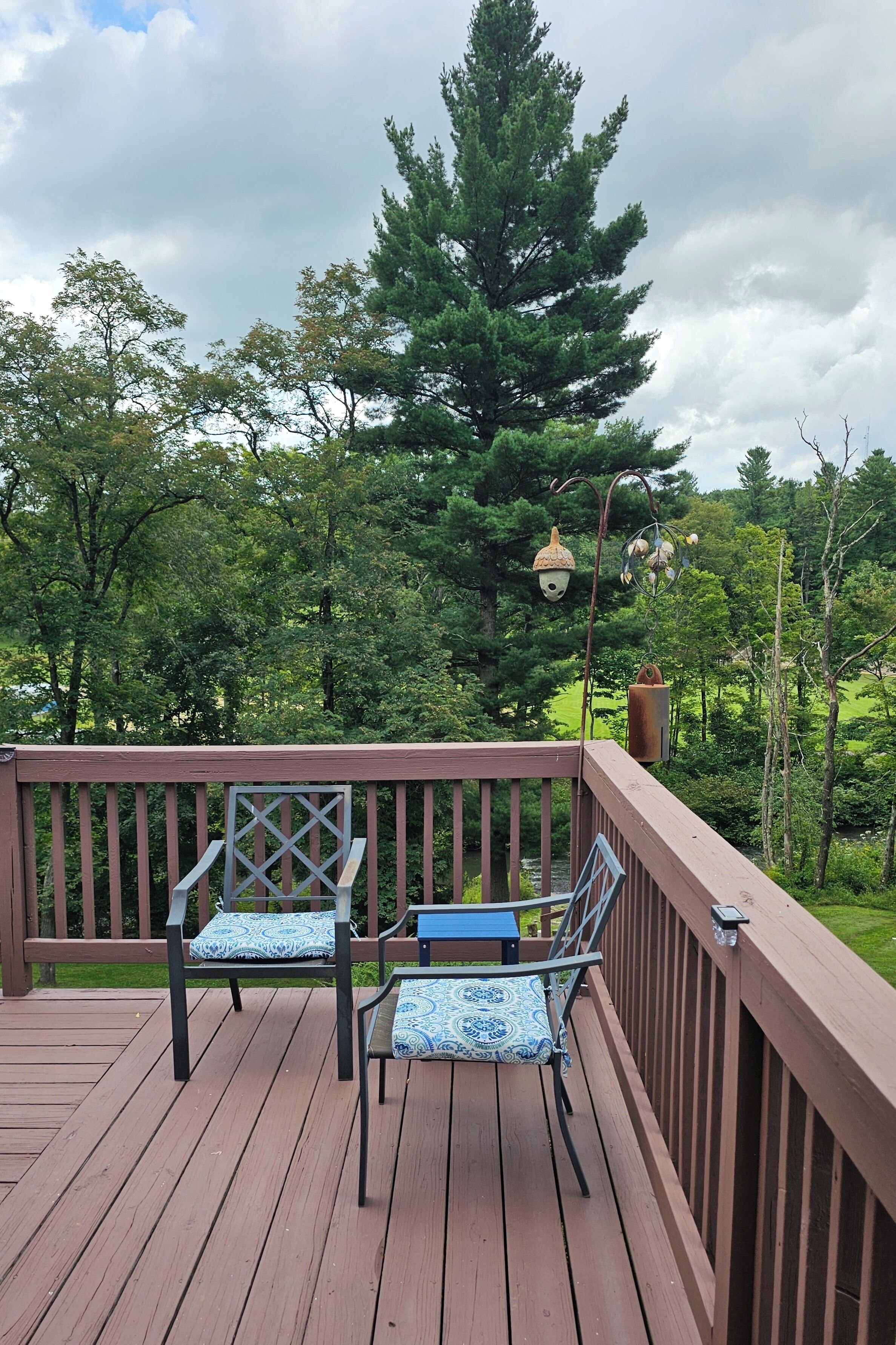 A wooden deck with two chairs and a table, surrounded by a railing, overlooking a forested area.