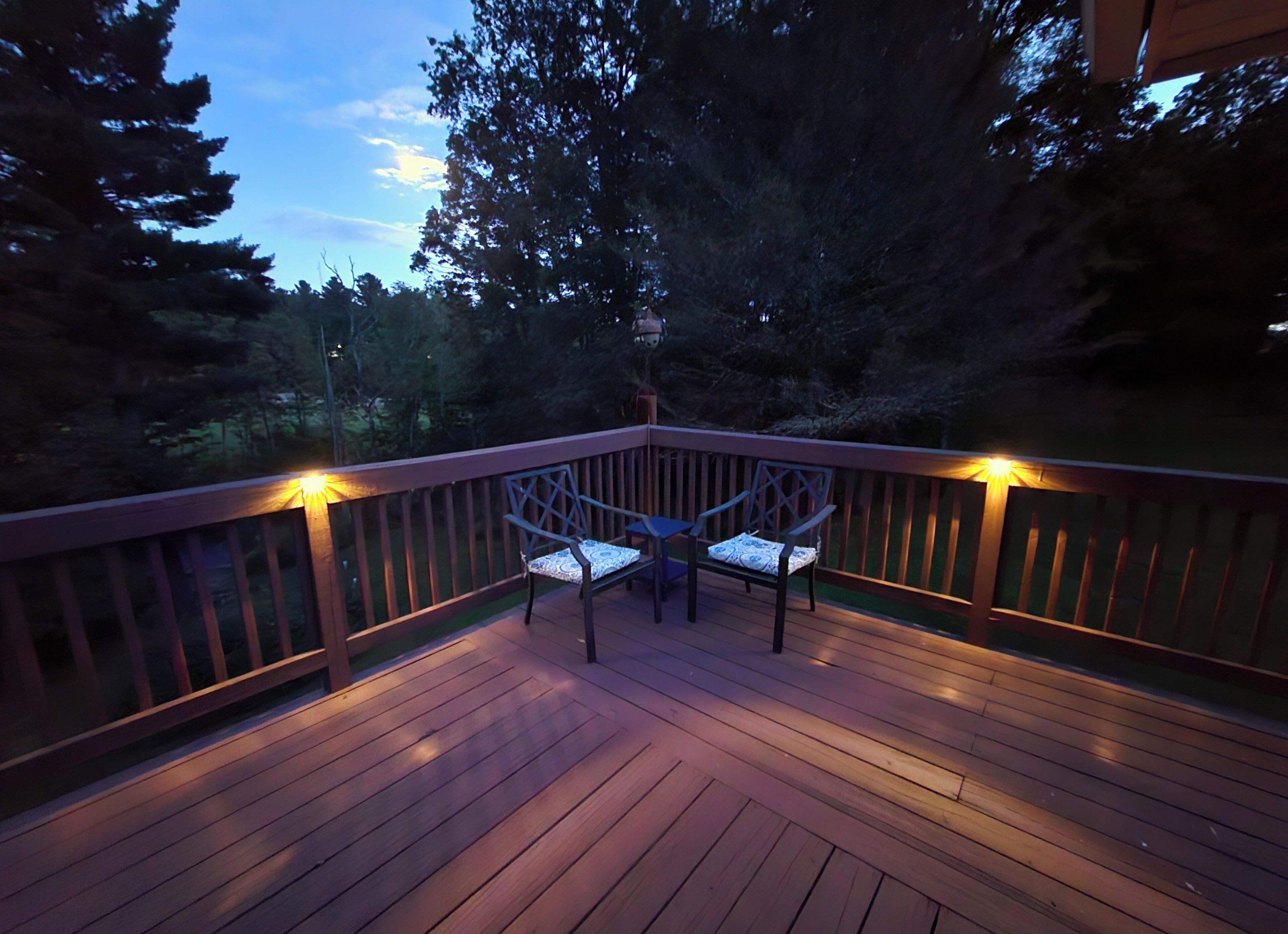 A wooden deck with two chairs and a table, surrounded by a railing and trees.