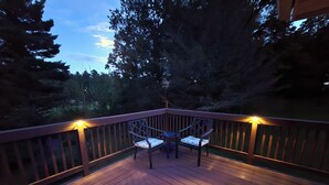 Une terrasse en bois avec deux chaises et une table, entourée d’une rambarde et d’arbres.