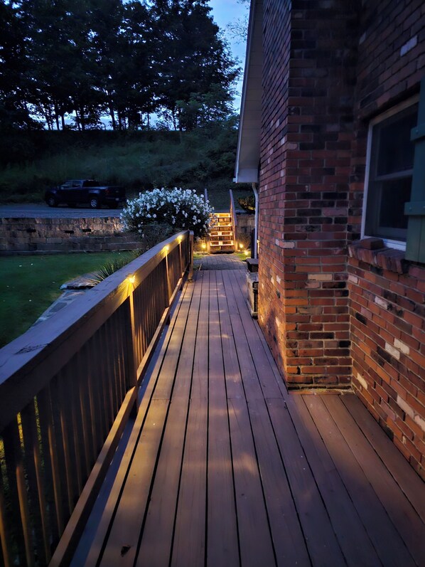 A wooden deck with a brick wall on one side, a metal railing, and a staircase leading to a covered area.