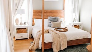 Une chambre à coucher avec un lit à baldaquin, une tête de lit en bois, du linge de lit blanc et un panier tressé posé sur le lit.