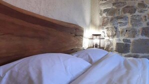 A bed with white linens in a room with a stone wall and a wooden headboard.