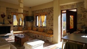 A stone-walled living room with a sofa set, a television, and a fireplace.