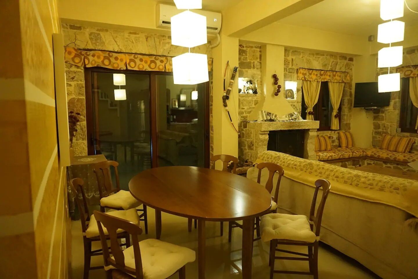 Een gezellig eetgedeelte met een ronde houten tafel en stoelen, een stenen openhaard en een comfortabele zithoek met gestreepte kussens.