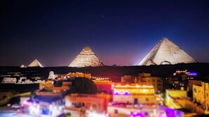 A nighttime view of a city with illuminated pyramids and a lit-up town square. - Golden Pyramids Inn (Giza)