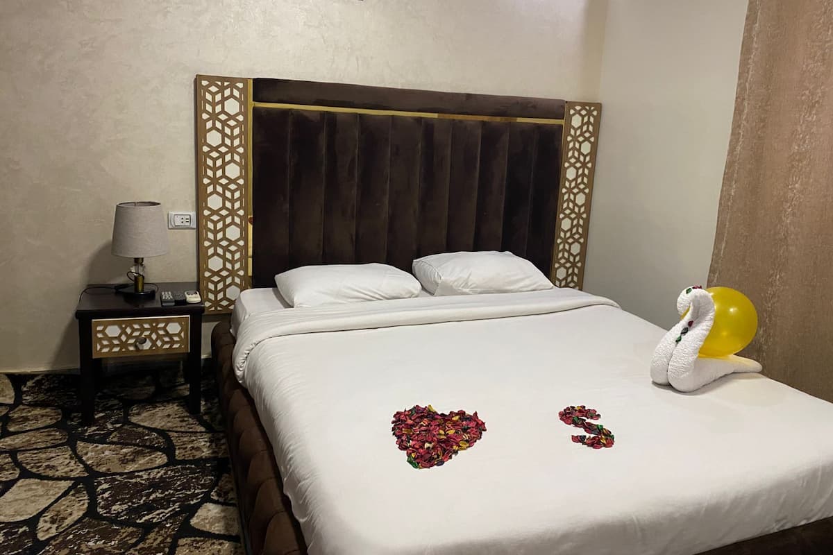 Quarto de hotel com cama, mesa de cabeceira, abajur e um balão decorativo.
