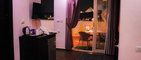 A hotel room with a bed, a desk with a telephone, a television, and a view of the outdoor area.