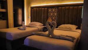Two beds with towels arranged in heart shapes, a headboard with a geometric pattern, and a wall-mounted lamp. - Golden Pyramids Inn (Giza)