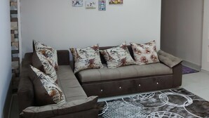A living room with a brown sofa and matching armchair, a patterned rug, and various wall art. - Golden Pyramids Inn (Giza)