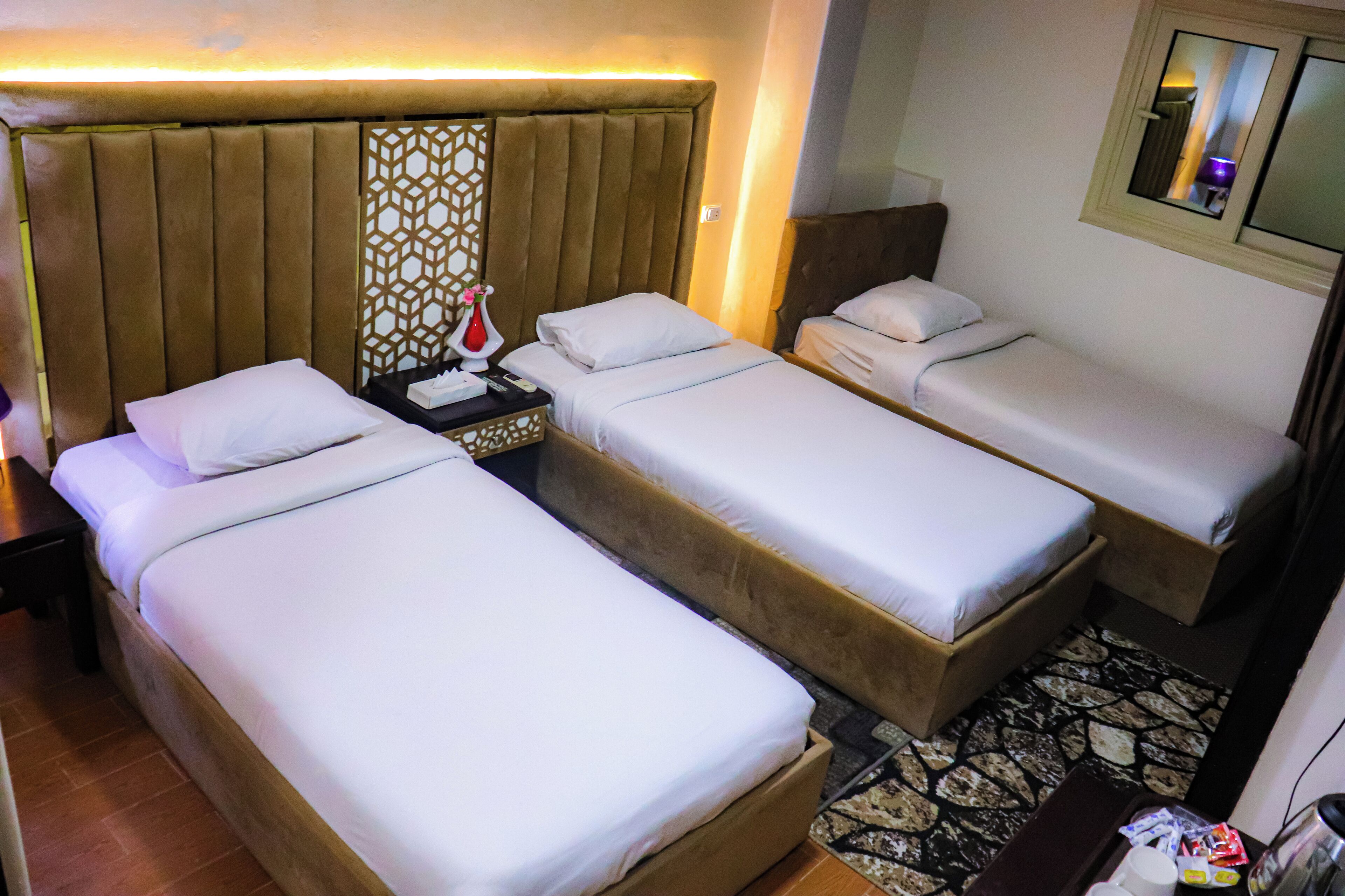A hotel room with two single beds, a nightstand, a decorative wall panel, and a small table with a lamp.
