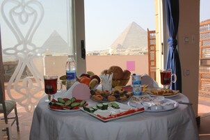 A table with a variety of food items, a glass of red beverage, and a bottle of water, with a view of pyramids in the background.