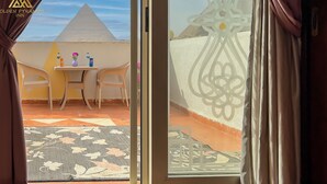 A room with a view of the Golden Pyramids, a small table with a vase and a bottle, and a patterned rug. - Golden Pyramids Inn (Giza)