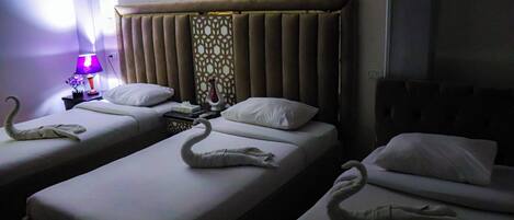 A hotel room with two single beds, each with a swan-shaped towel. There is a nightstand with a lamp and a decorative item.