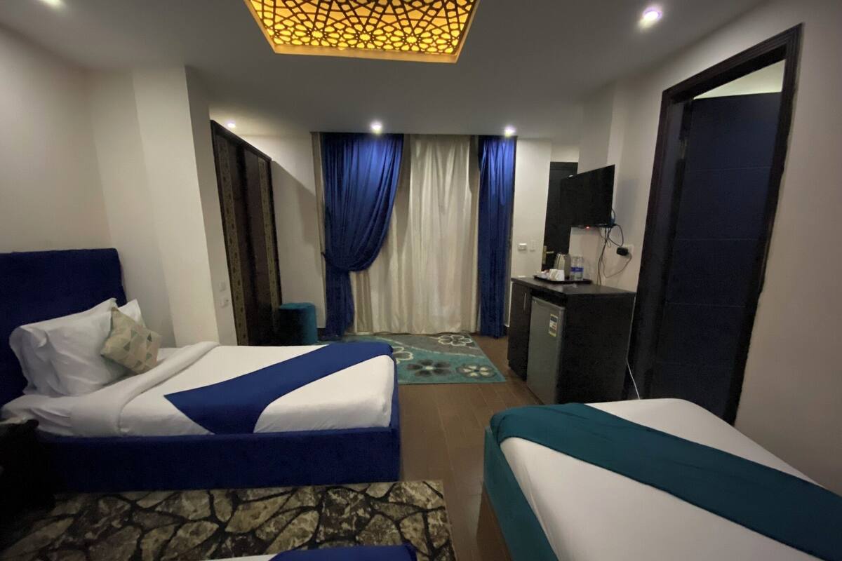 Quarto de hotel com duas camas, uma escrivaninha, uma televisão e um minibar.