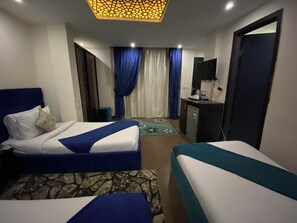 A hotel room with two beds, a desk, a TV, and a minibar.