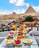 A table set with various dishes and drinks, overlooking a cityscape with pyramids in the background.