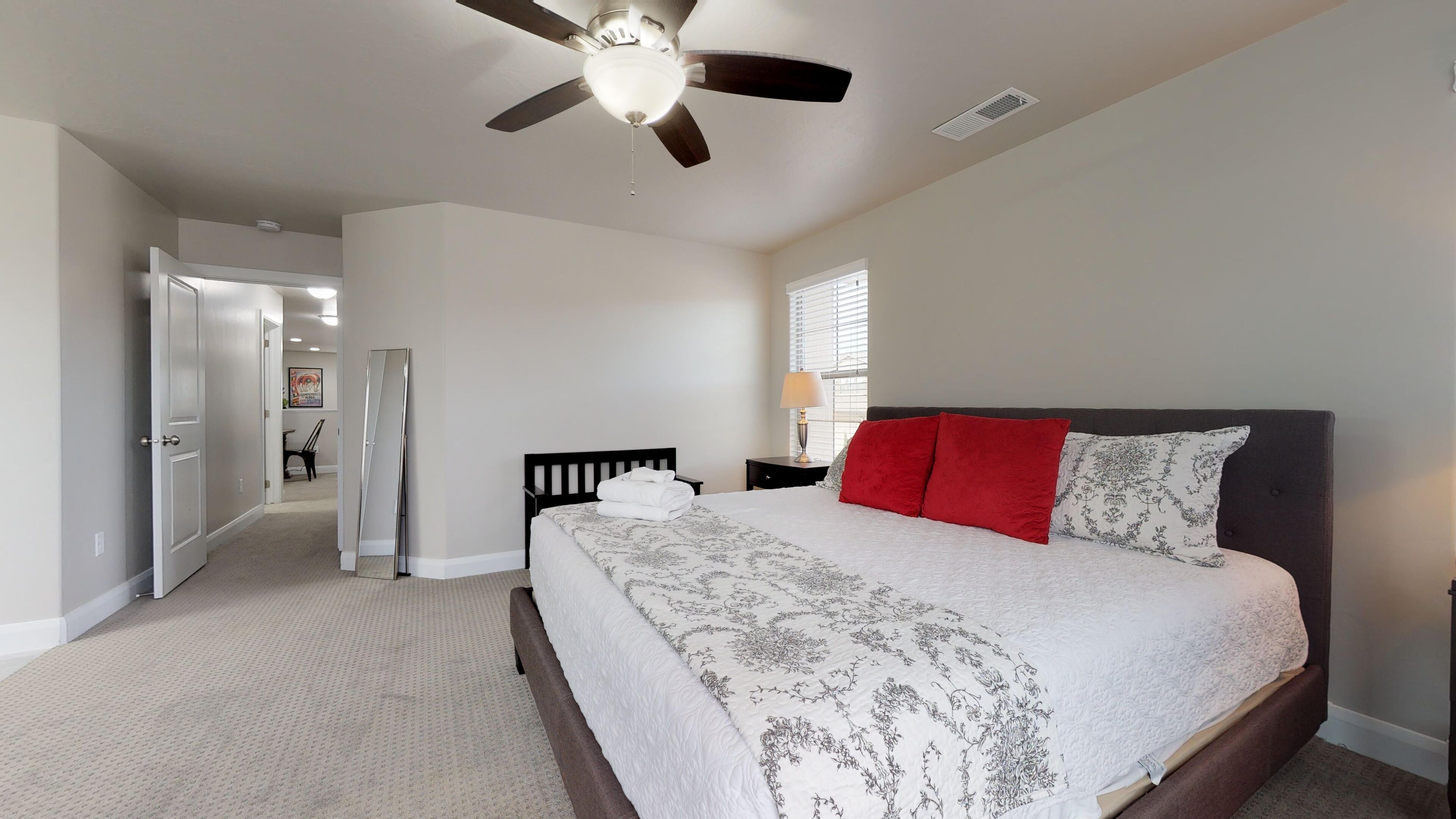 Une chambre à coucher comprenant un lit, un ventilateur de plafond, une fenêtre avec des stores et une porte donnant sur une autre pièce.