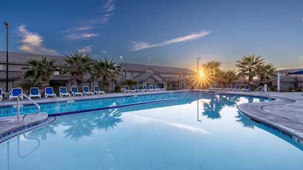 Une piscine entourée de bâtiments, agrémentée de chaises longues et de palmiers.