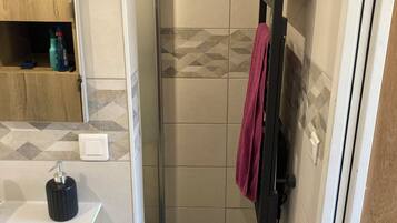 A bathroom with a shower, a wooden cabinet, a black soap dispenser, and a towel rack with a red towel.