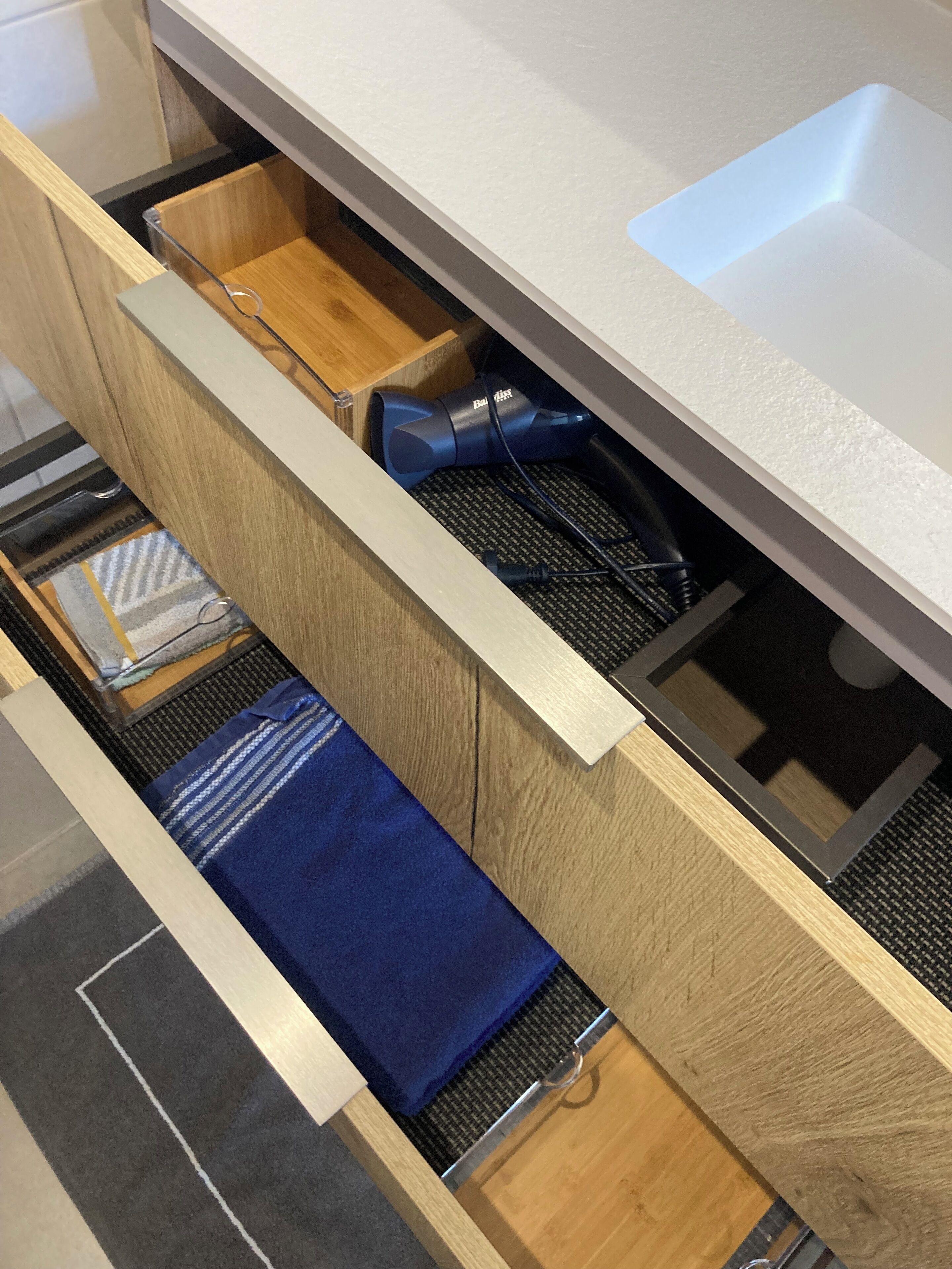 A kitchen drawer with a blue towel, a black appliance, and a white sink.