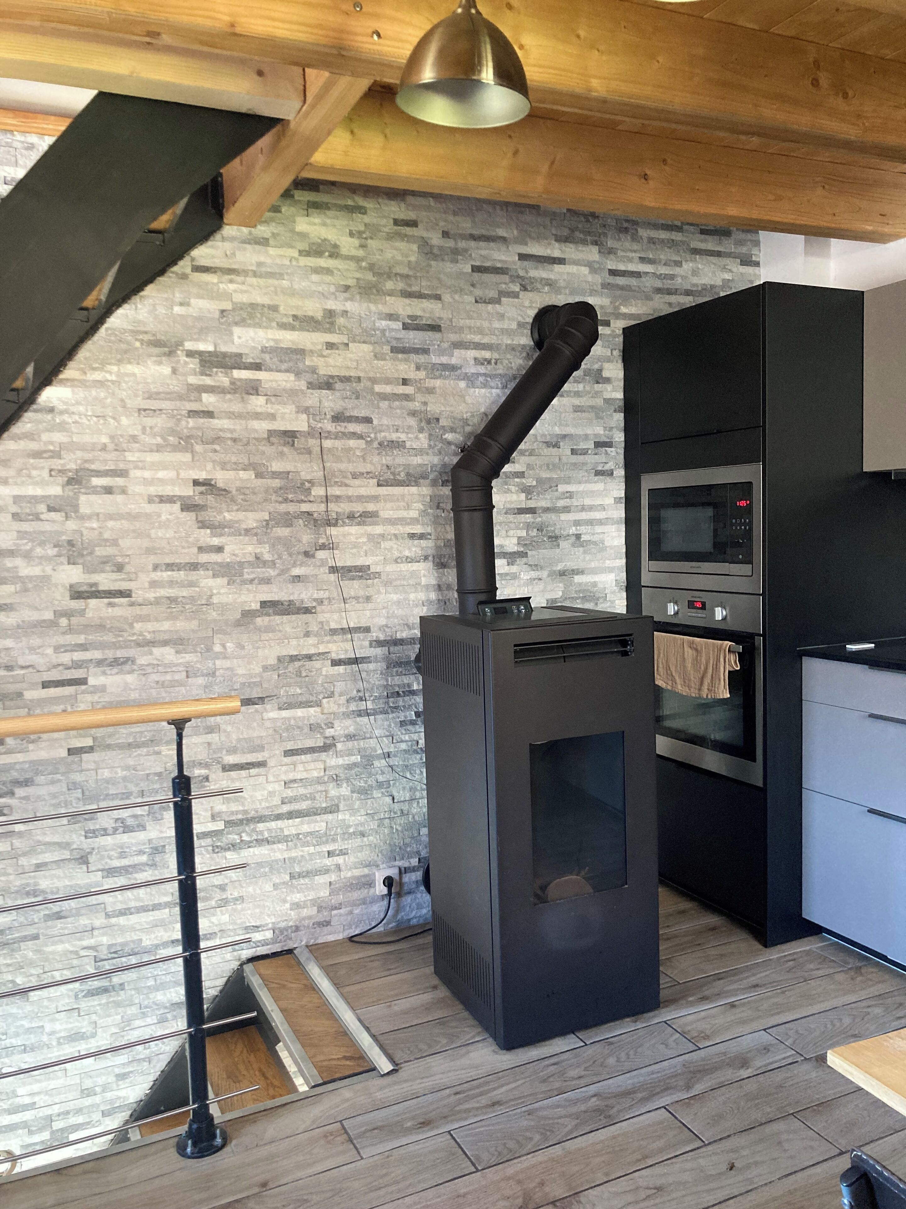 Une cuisine moderne dotée d’un poêle à bois, d’un four encastré et d’un pare-feu en pierre.