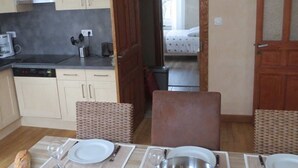Un comedor con una mesa lista para cuatro, una cocina al fondo y un dormitorio visible a través de una puerta abierta.