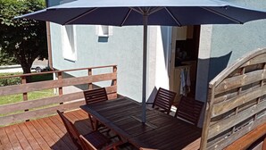 Una terraza de madera con una mesa, sillas y un paraguas, junto a una valla de madera.