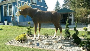 Une sculpture d’un élan dans un jardin, avec une maison bleue en arrière-plan.