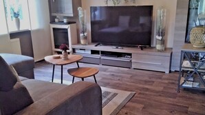 Un salon moderne avec un grand téléviseur à écran plat, un canapé gris, une petite table ronde et une table basse.