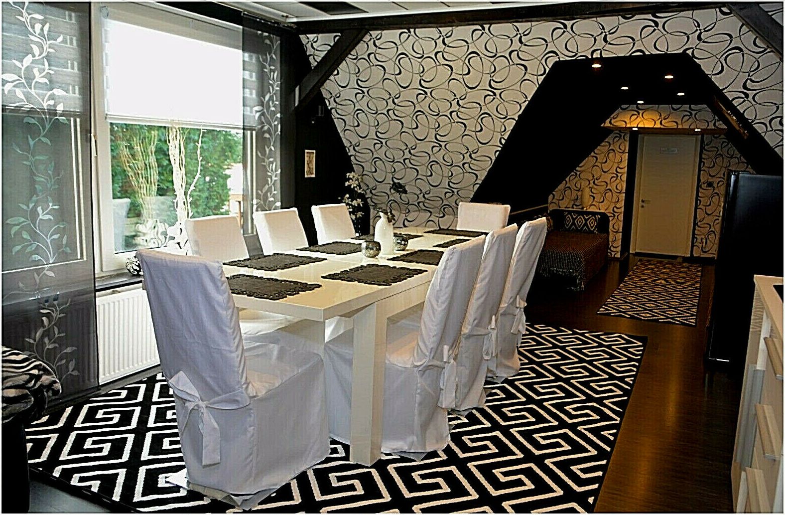 Un coin repas avec une table dressée pour six personnes, des chaises blanches et un sol à motifs.