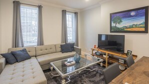 Ein Wohnzimmer mit einer Couch, einem Couchtisch, einem Fernseher und einem Bild an der Wand.