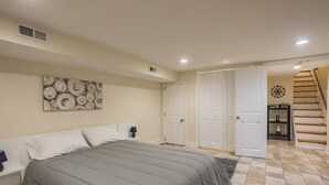 Ein Schlafzimmer mit einem Bett, einem Nachttisch, einer Wanduhr und einer Tür, die zu einer Treppe führt.