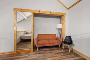 A room with a wooden-framed doorway leading to a bedroom, a sofa, a lamp, and a chair. - SnowPine Condo, Sleeps 8, A/C, Fireplace (Ellicottville)