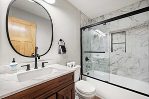 A bathroom with a large mirror, a wooden vanity, a white sink, a toilet, and a glass-enclosed shower area. - SnowPine Condo, Sleeps 8, A/C, Fireplace (Ellicottville)