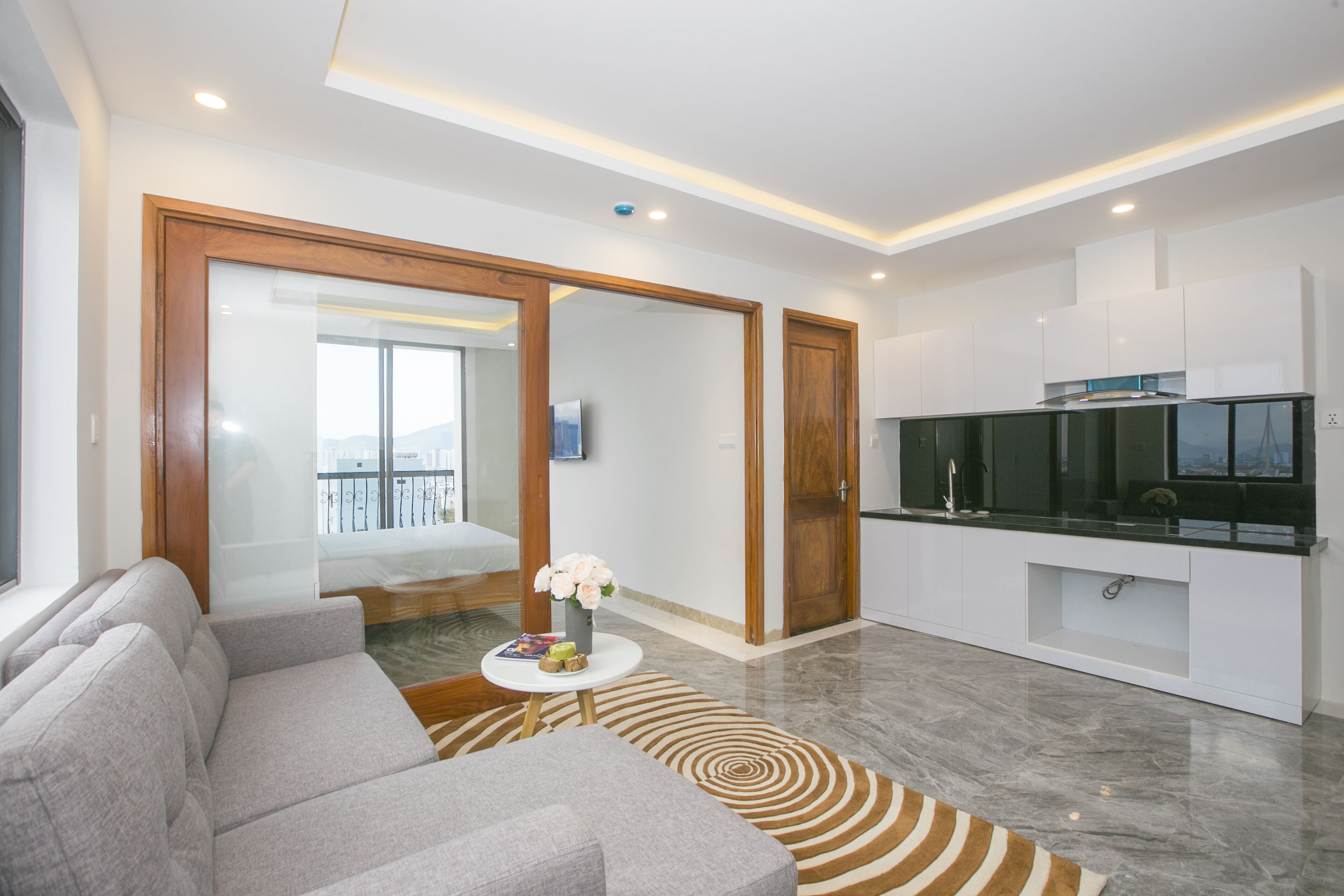 A modern living room with a grey sofa, a small round table with a vase of flowers, and a TV on a black stand.