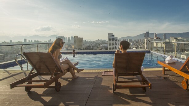 Un área de piscina en la azotea con sillones de descanso y vistas a un paisaje urbano.