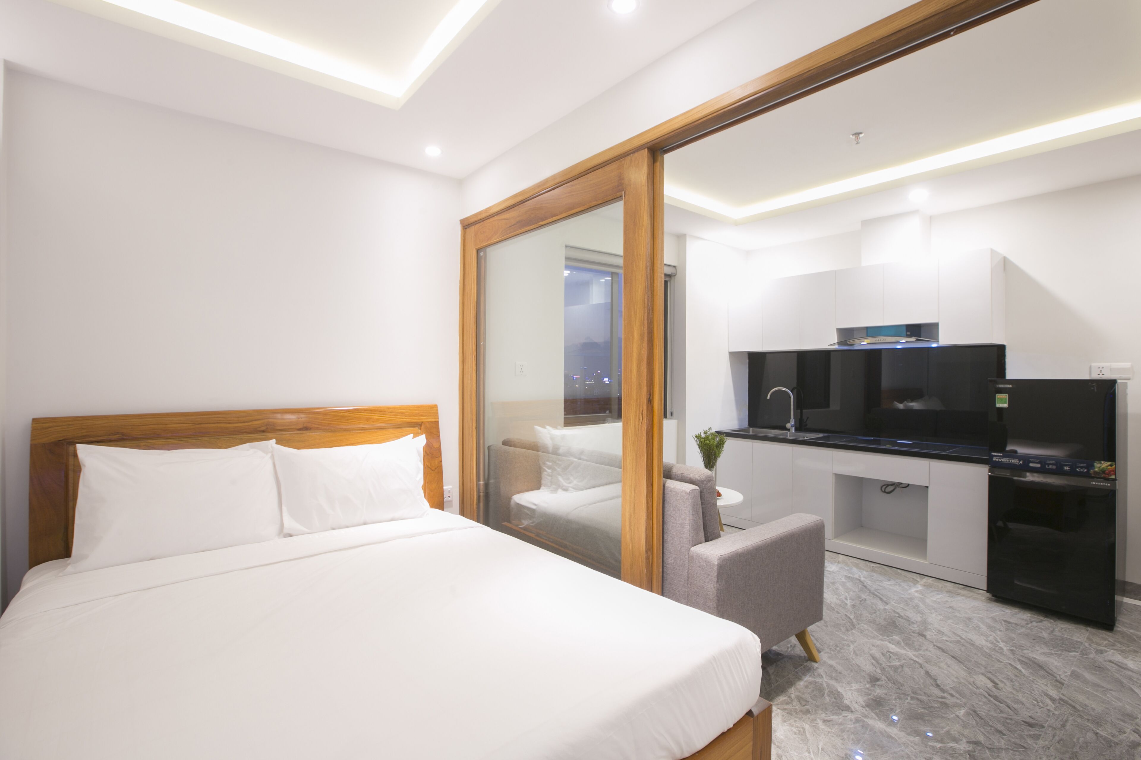 A hotel room with a bed, a seating area, a kitchenette, and a large mirror.