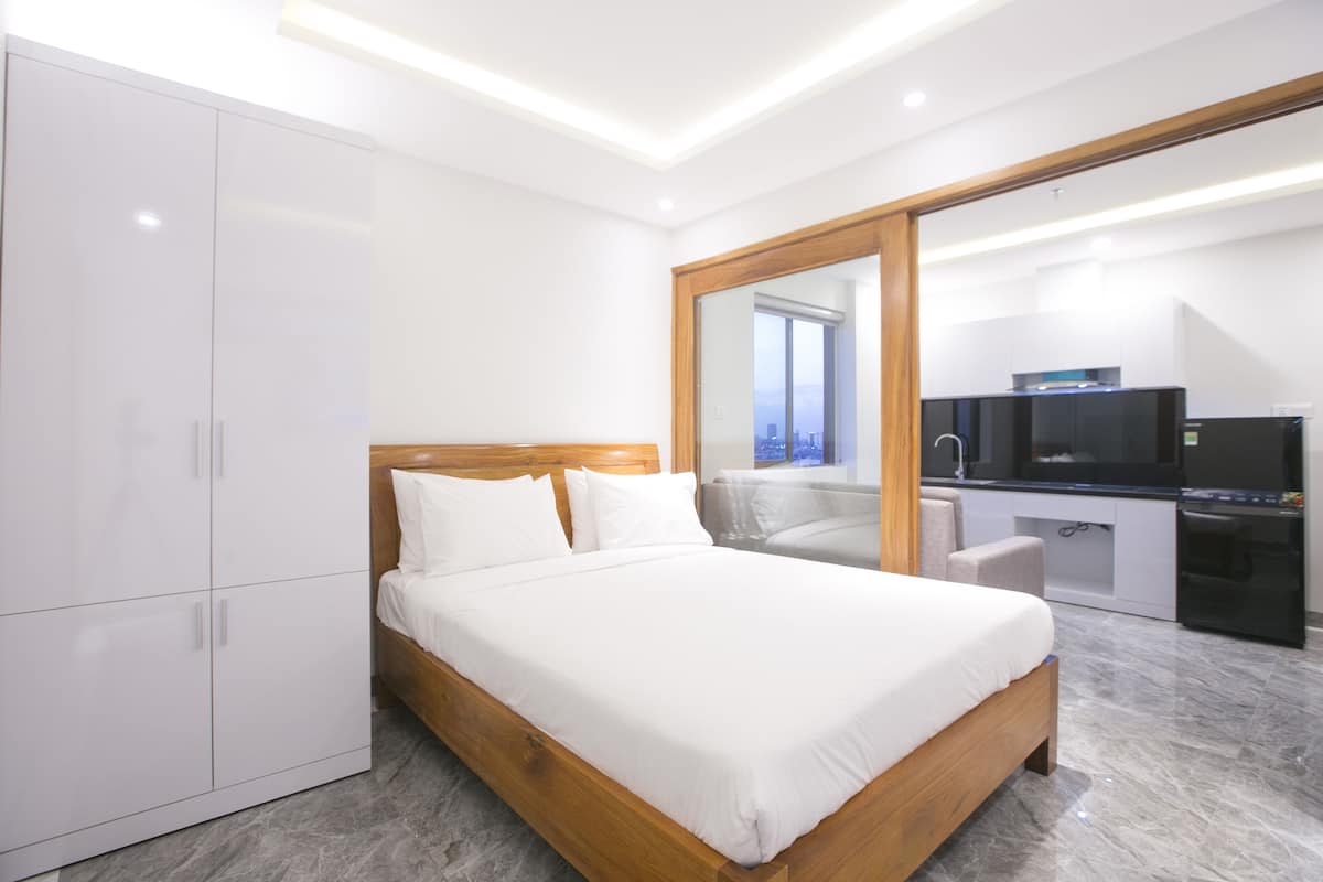 Une chambre moderne avec un grand lit, une armoire et une vue sur le paysage urbain, visible à travers une porte vitrée.