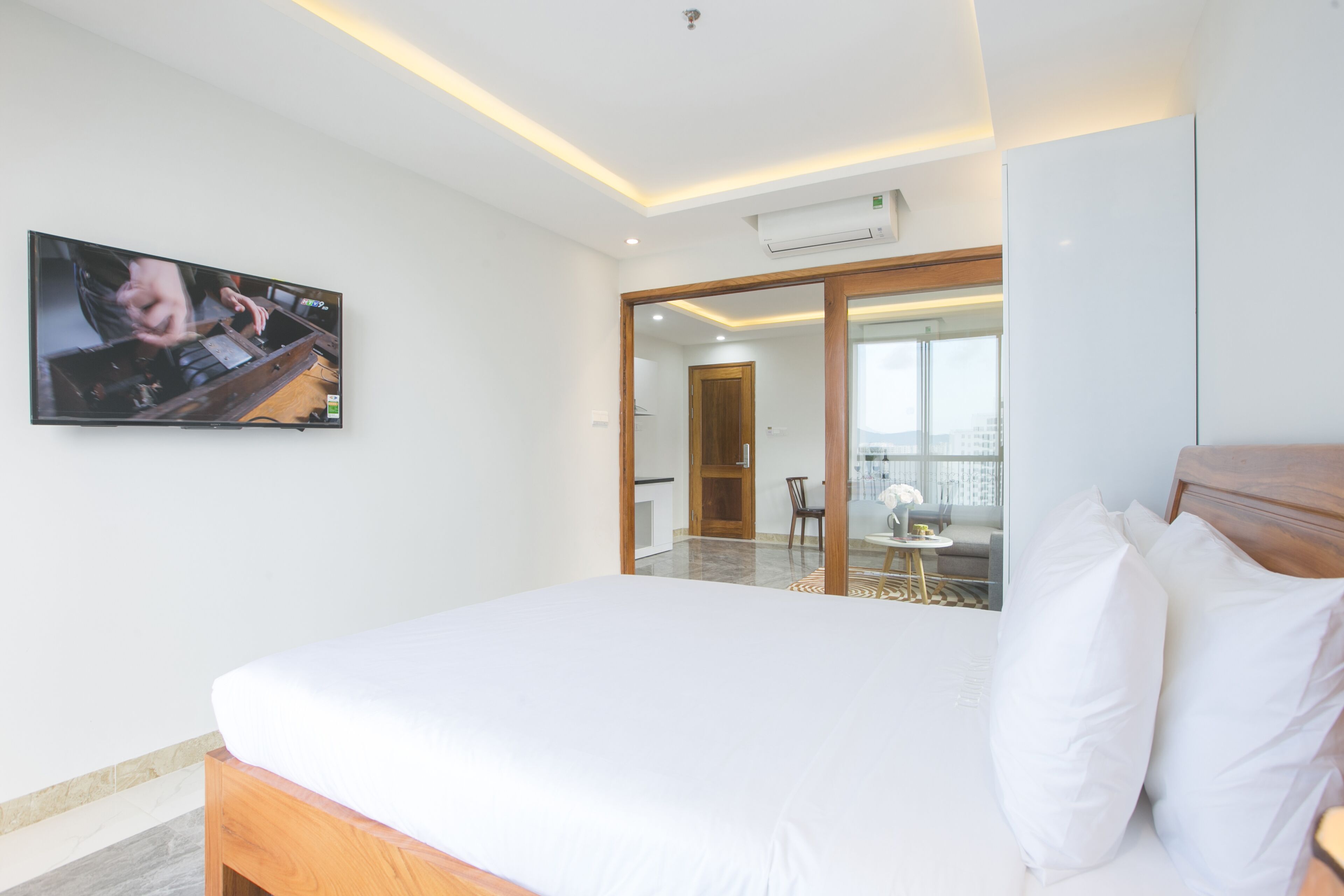 A hotel room with a large bed, a flat-screen TV mounted on the wall, and a sliding glass door leading to a balcony.