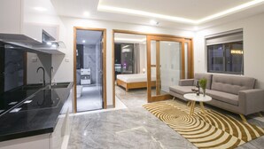 Una habitación de hotel moderna con cocina, sofá, una pequeña mesa con un florero y una cama.