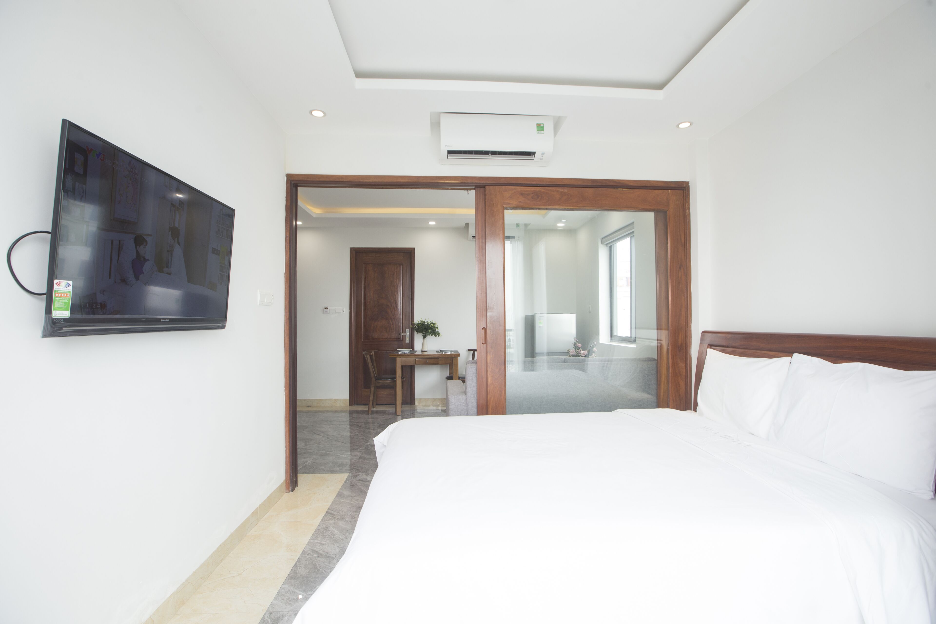 Habitación de hotel con una cama grande, un televisor de pantalla plana montado en la pared, una puerta de madera y un equipo de aire acondicionado en el techo.