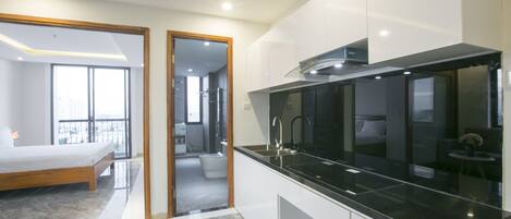 A modern hotel room with a large bed, a separate bathroom, and a kitchen area with a black countertop.