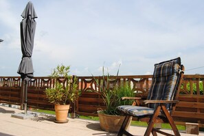 A wooden deck with a metal chair and an umbrella, surrounded by potted plants. - Time out in the Rheinhessen vineyards (Hackenheim)